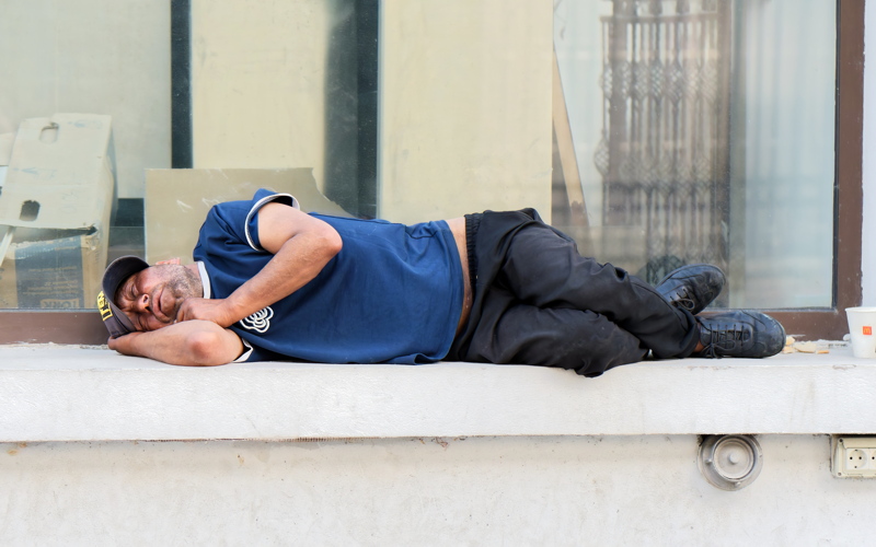 22 - Person resting on a ledge, illustrating the difficult circumstances faced by those experiencing homelessness